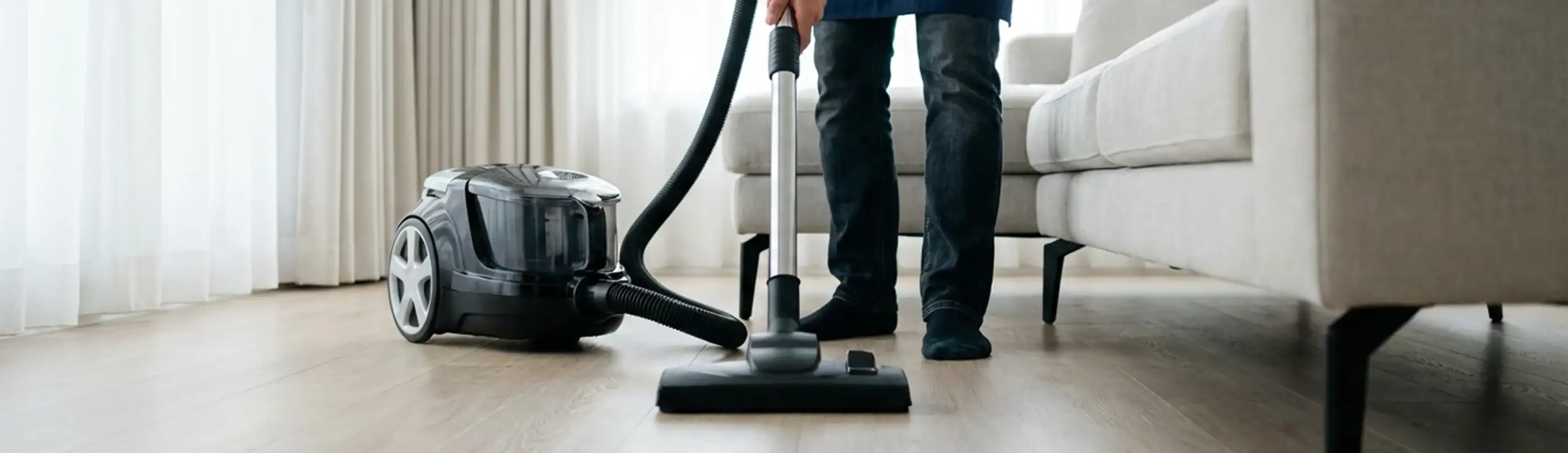 Professional house cleaner vacuuming a living room floor with a canister vacuum cleaner, Baton Rouge, LA.