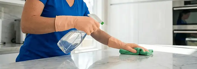 Maid service worker spraying and wiping a kitchen countertop with a microfiber cloth for sanitizing, Baton Rouge, LA.
