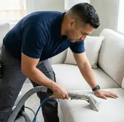 Professional upholstery cleaning technician using an extraction wand to deep-clean a fabric sofa, Baton Rouge, LA.