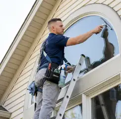 Professional window cleaner on a ladder using a squeegee to clean an exterior arched window, Baton Rouge, LA.