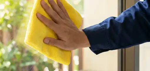House cleaner wiping a glass window with a yellow microfiber cloth for streak-free cleaning, Baton Rouge, LA.